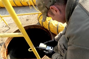 Worker crouching over an open manhole holding a gas monitor