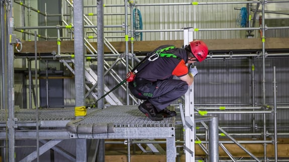 Man wearing a harness and hard hat crouching on the edge of a platform, doing Leading edge fall protection training