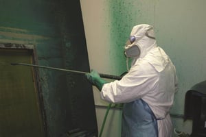 worker wearing disposable white coveralls holding a pressure washer wand