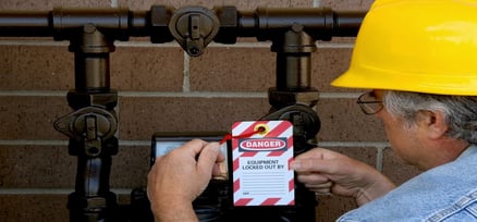 Man standing in front of pipes securing a lockout tag to a valve