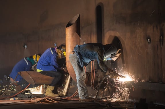 Welders in a dimly lit tunnel welding large pipes