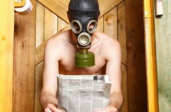 Man sitting shirtless in front of a wooden door holding a newspaper and wearing a gas mask