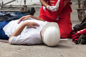 Worker lying on the ground while a First Aid responder kneels next to him unrolling gauze