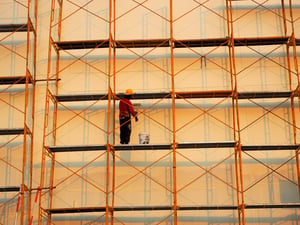 Man standing on scaffolding next to a tall building