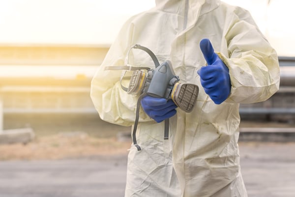 worker wearing white coveralls and blue chemical gloves holding a respirator mask