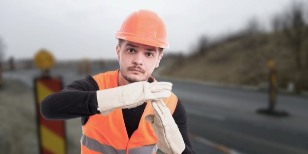 man wearing a safety vest and hard hat holding his hands up to signal "stop"